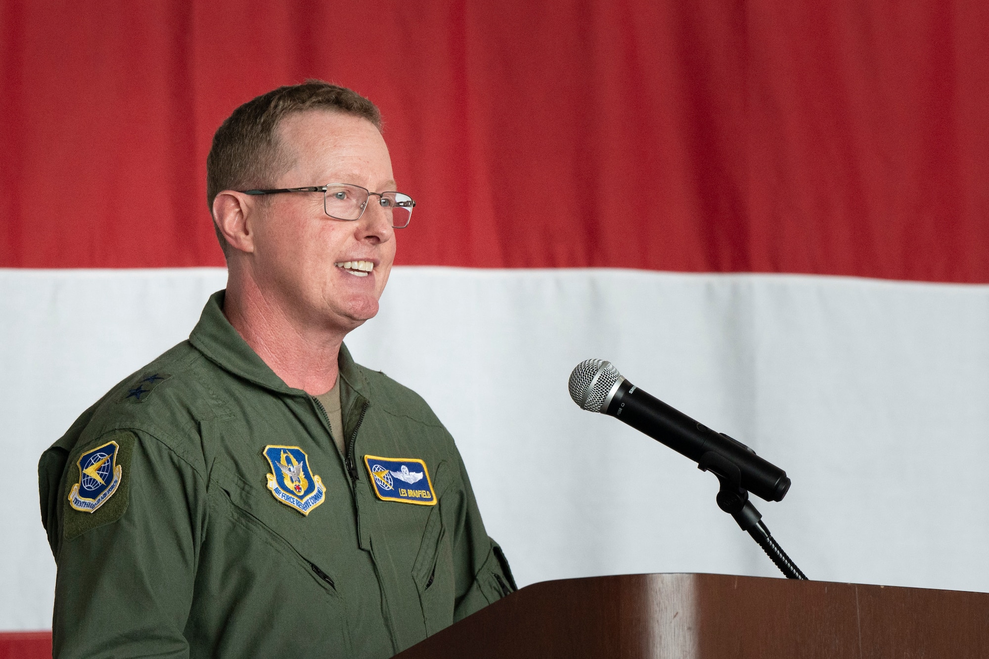 a man in a military uniform speaks into a microphone while standing in front of an American flag