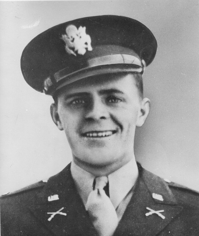 A man in a military dress uniform and cap smiles for a photo.