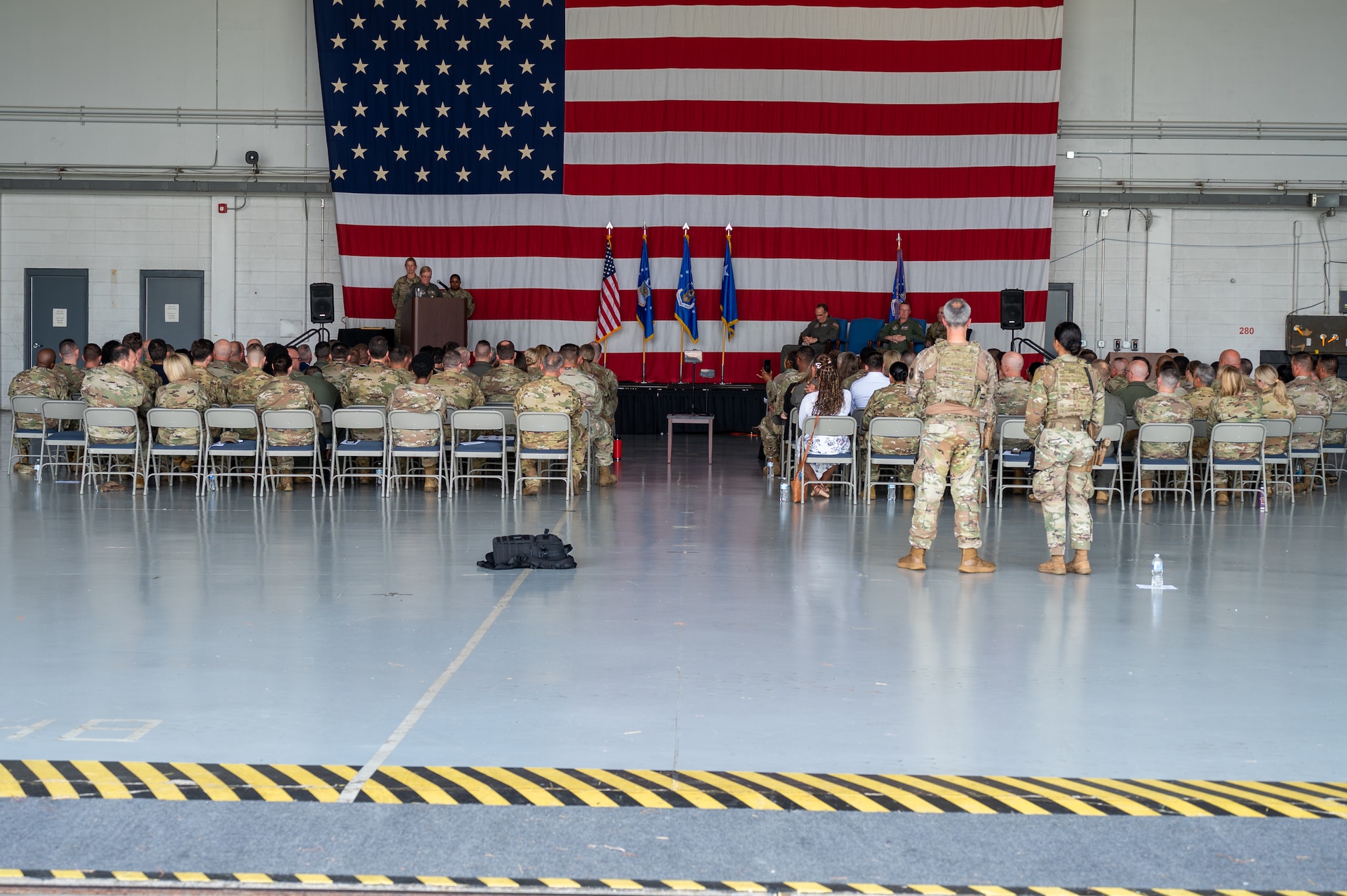 people in military uniforms sit in chairs while looking toward a stage and American flag