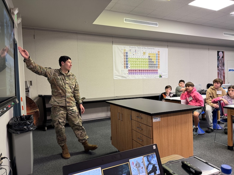 Man in uniform pointing to a screen while lecturing to students.