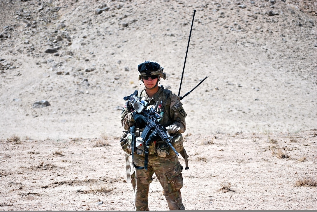 Man in uniform holding a gun in the desert.