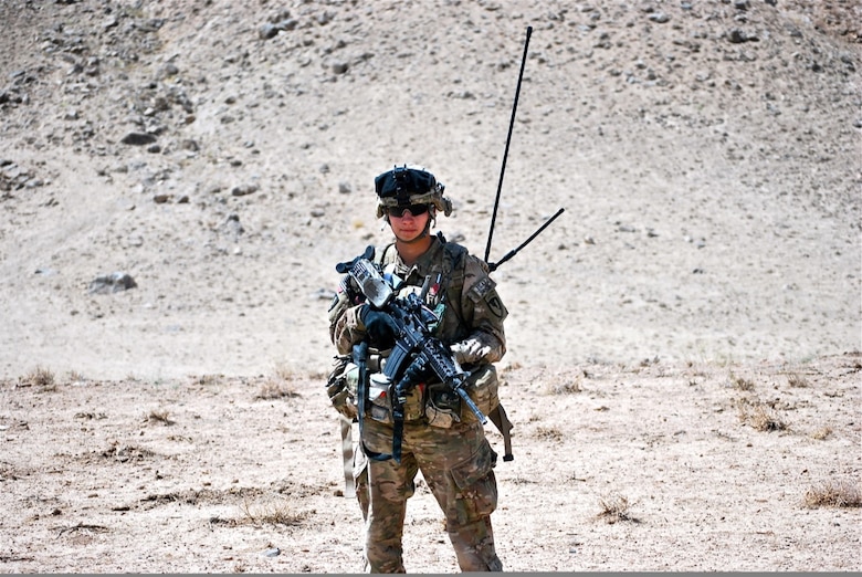 Man in uniform holding a gun in the desert.