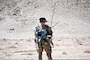 Man in uniform holding a gun in the desert.