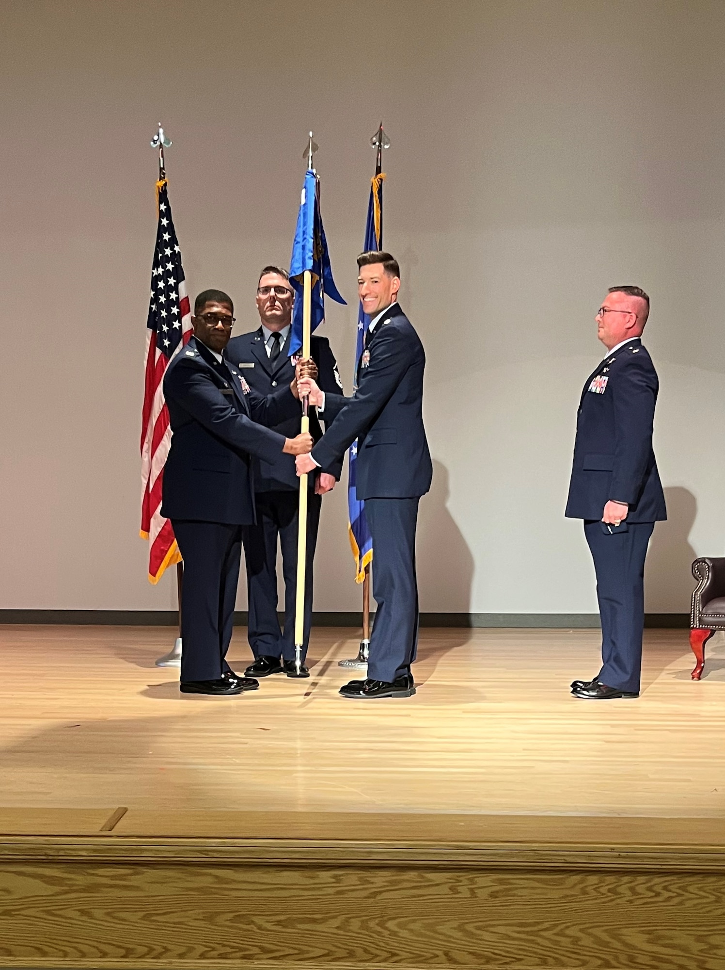 photo of four uniformed US Airmen standing on a stage, two Airmen are holding a unit flag in between them