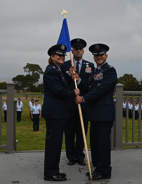 U.S. Air Force Col. Mark Jones, outgoing 517th Training Group commander, passes the guidon to Col. Angelina Maguinness, 17th Training Wing commander, relinquishing command during the change of command ceremony on Soldier Field at Presidio of Monterey, California, June 12, 2025. Passing the guidon represents the transfer of leadership responsibilities to the next commander. (U.S. Air Force photo by Staff Sergeant Nathan Call)