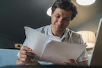 Man in white shirt reads papers while smiling.
