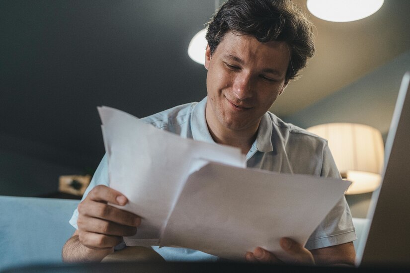 Man in white shirt reads papers while smiling.