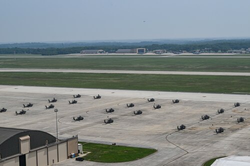 U.S. Army AH-64 Apache and UH-60 Black Hawk helicopters are parked on the flight line.