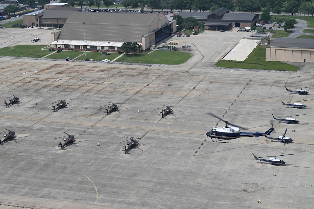 U.S. Air Force UH-1N Huey helicopter assigned to the 1st Helicopter Squadron flies over parked UH-1N Huey and U.S. Army AH-64 Apache helicopters.