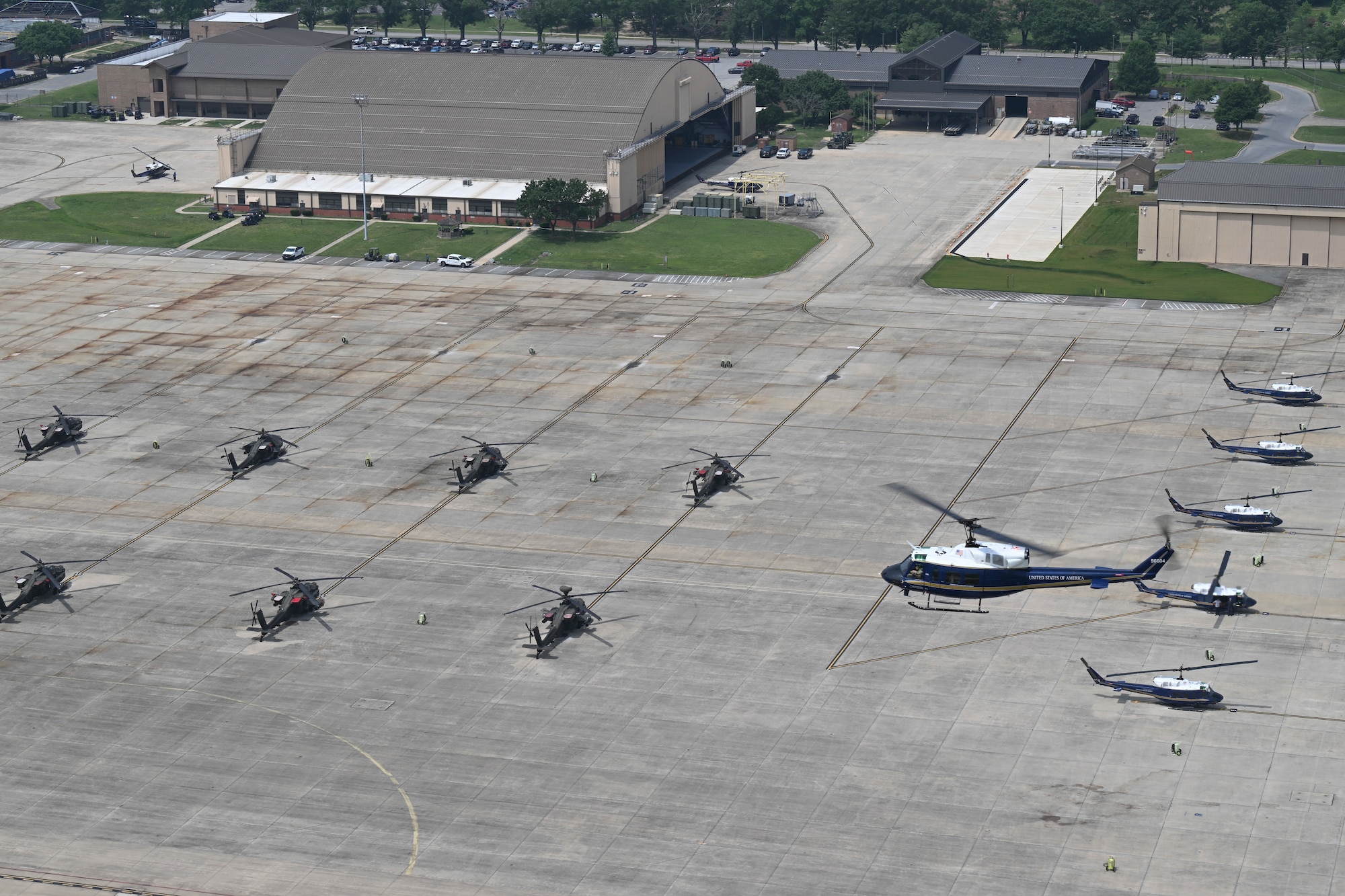 U.S. Air Force UH-1N Huey helicopter assigned to the 1st Helicopter Squadron flies over parked UH-1N Huey and U.S. Army AH-64 Apache helicopters.