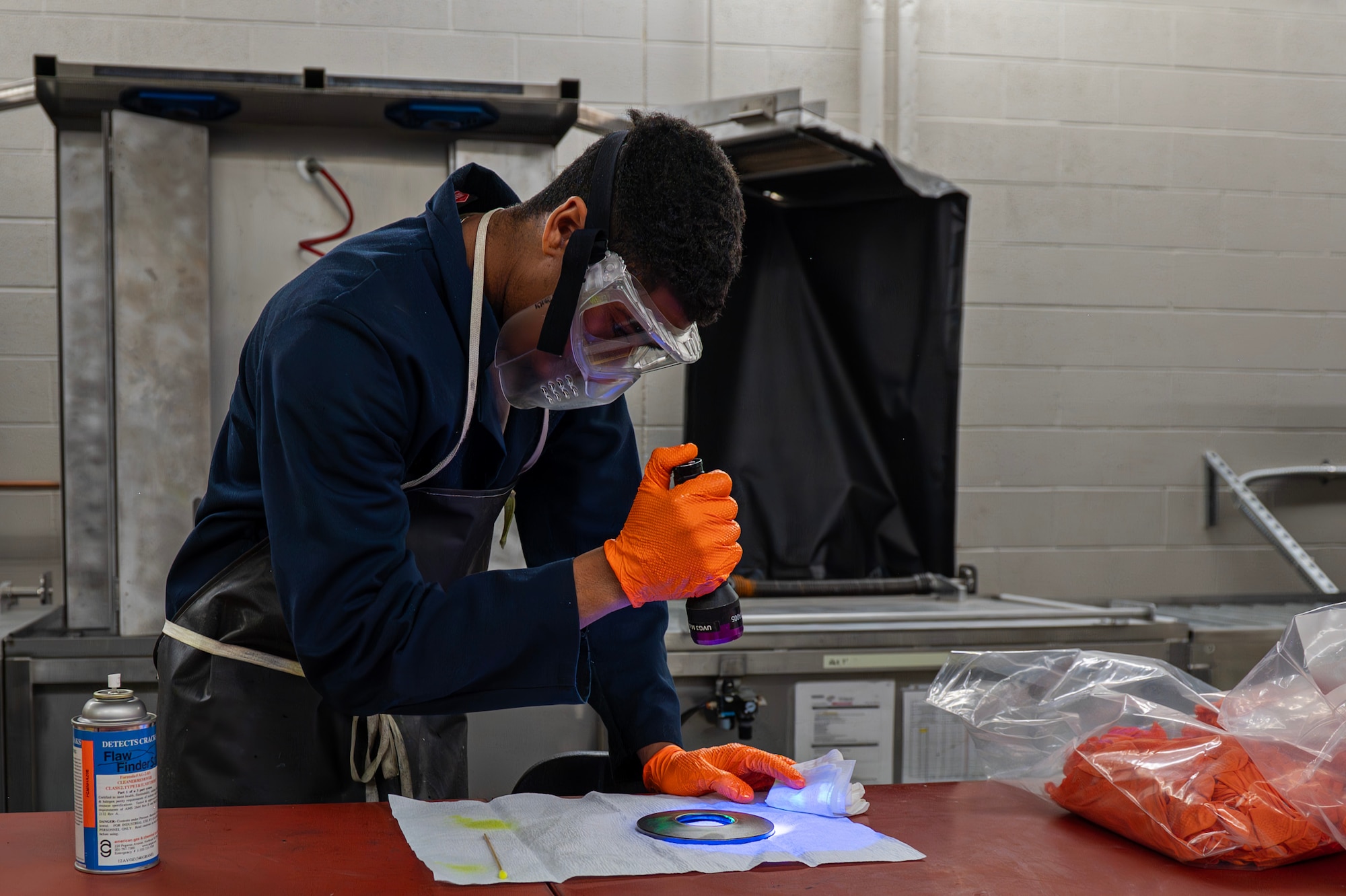 U.S. Air Force Senior Airman Amare Francois, 92nd Maintenance Squadron nondestructive inspection technician, shines an ultraviolet light on a piece of equipment at Fairchild Air Force Base, Washington, June 12, 2025. The fluorescent dye in the penetrant Francois rubbed onto the equipment glowed brightly under ultraviolet light, allowing him to see flaws that would otherwise be invisible to the naked eye. (U.S. Air Force photo by Senior Airman St Marks)