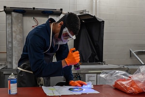 U.S. Air Force Senior Airman Amare Francois, 92nd Maintenance Squadron nondestructive inspection technician, shines an ultraviolet light on a piece of equipment at Fairchild Air Force Base, Washington, June 12, 2025. The fluorescent dye in the penetrant Francois rubbed onto the equipment glowed brightly under ultraviolet light, allowing him to see flaws that would otherwise be invisible to the naked eye. (U.S. Air Force photo by Senior Airman St Marks)