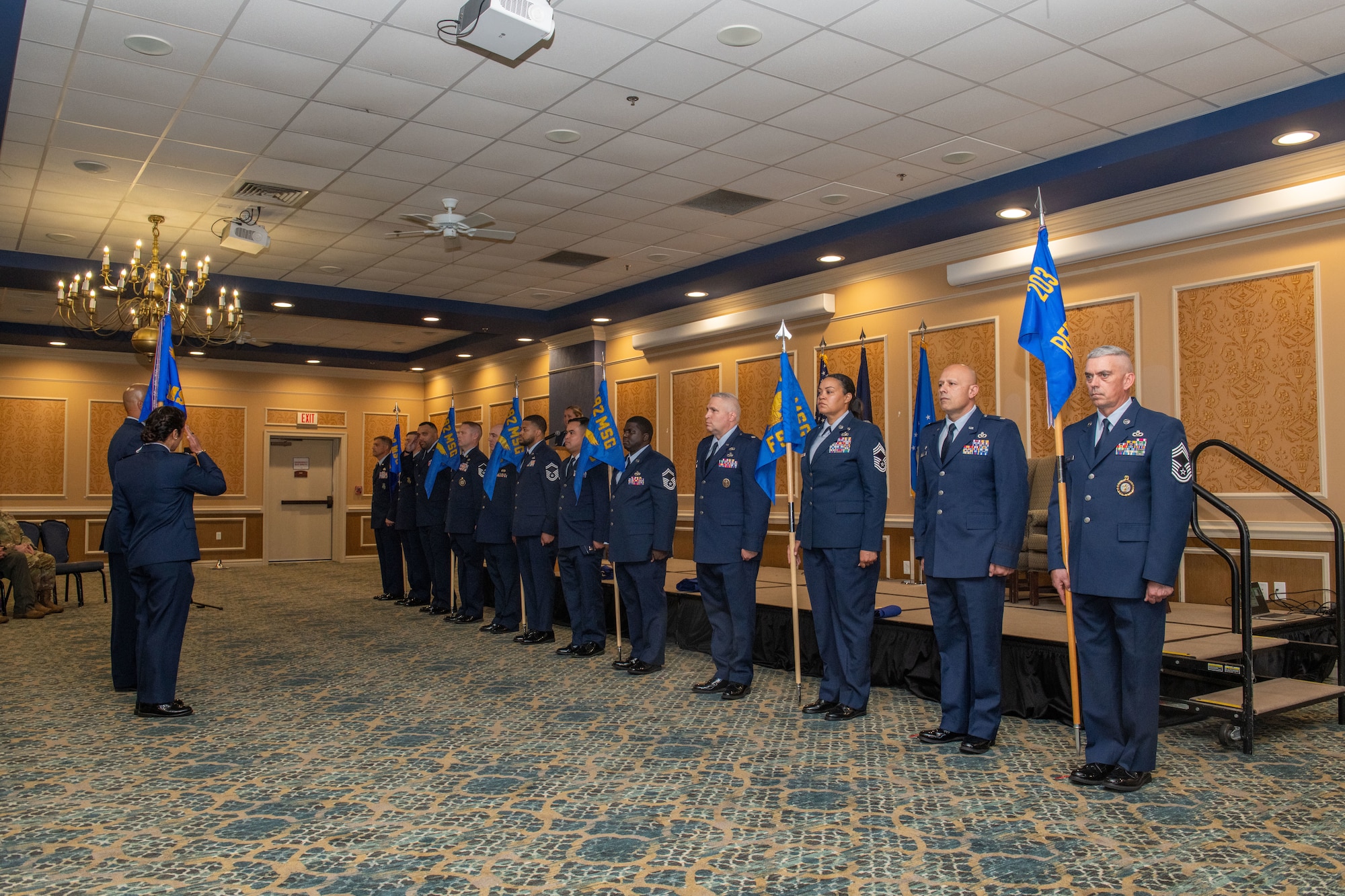 12 senior leaders with the 192nd Mission Support Group stand in a row holding guidons from each flight and squadron; MSG commander and senior enlisted leader stand facing them