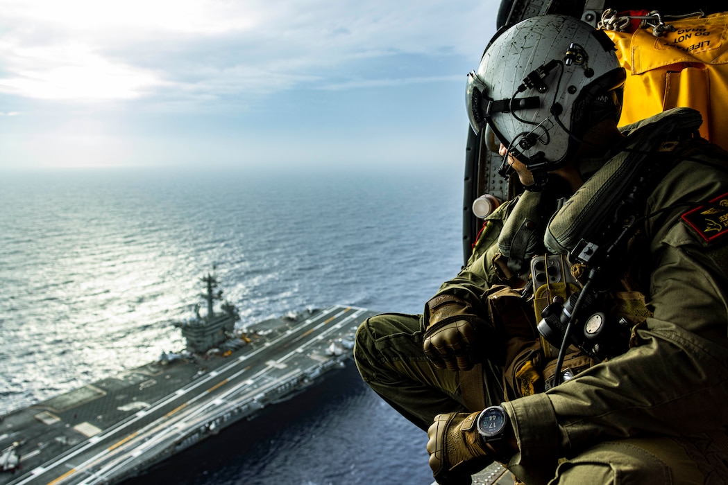 Naval Air Crewman (Helicopter) 2nd Class Jeremy Valdez from Kaneohe, Hawaii, assigned to the Golden Falcons of Helicopter Sea Combat Squadron (HSC) 12, looks down at Nimitz-class aircraft carrier USS George Washington (CVN 73) in an MH-60S Seahawk while underway in the Philippine Sea, June 15, 2025.