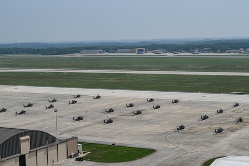 U.S. Army AH-64 Apache and UH-60 Black Hawk helicopters are parked on the flight line.
