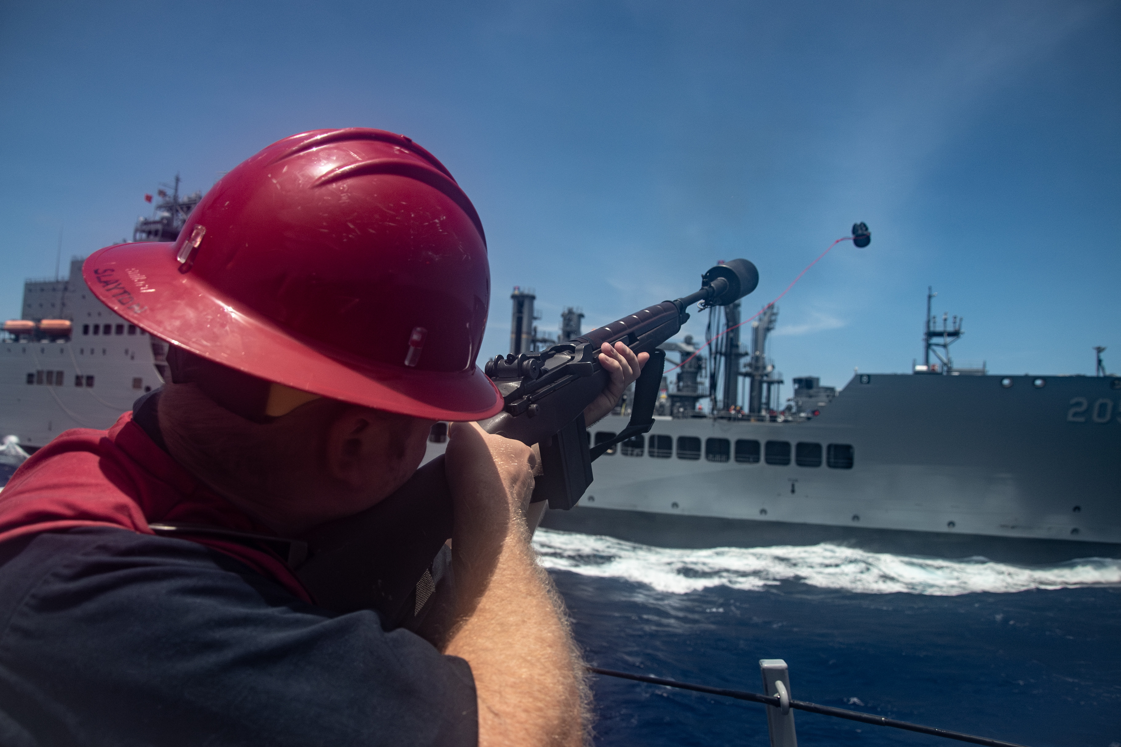 A Sailor fires the shot line to the fleet replenishment oiler USNS John Lewis (T-AO 205) during an underway replenishment from the fo'c'sle of the Arleigh Burke-class guided-missile destroyer USS Gridley (DDG 101) in the South China Sea, June 13, 2025. The Gridley, assigned to the Nimitz Carrier Strike Group, is underway in the U.S. 7th Fleet area of operations on a scheduled deployment, demonstrating the U.S. Navy's unwavering commitment to a free and open Indo-Pacific. (U.S. Navy photo by Mass Communication Specialist 2nd Class Timothy Meyer)