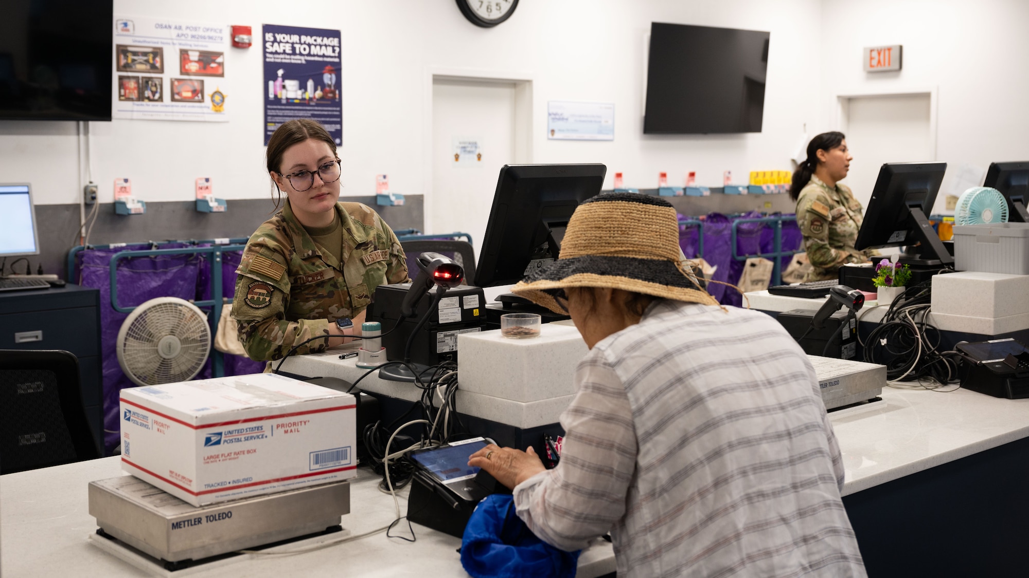 U.S. Air Force Airman 1st Class Hanna Tucker, 51st Force Support Squadron military postal clerk, assists a customer with shipping at Osan Air Base, Republic of Korea, June 16, 2025. The goal of Airmen at the post office is to provide excellent customer service to the community by answering questions they may have as well as assisting in sending and receiving packages. (U.S. Air Force photo by Senior Airman Rome Bowermaster)