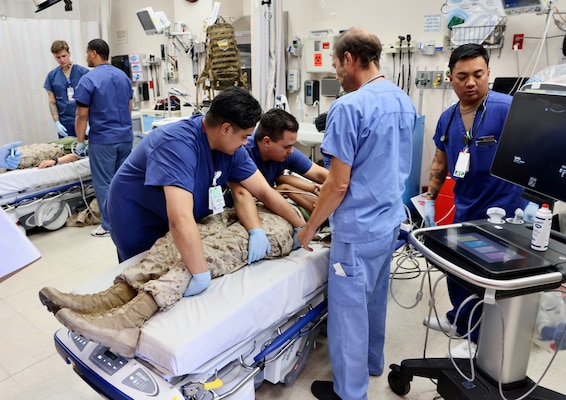 Emergency Department personnel at Naval Hospital Twentynine Palms conduct triage and initiate treatment on two role-playing Marines with simulated critical injuries during the Semper Durus 2025 regional training exercise, May 21. The casualties arrived via air medical evacuation following a notional explosion and friendly fire incident on Range 112, part of a mass casualty scenario coordinated with Marine Corps Air Ground Combat Center (MCAGCC) and other base tenants. After being transferred from the helipad by a corpsman and duty driver, the simulated patients were brought through the ambulance entrance, where medical teams activated the hospital’s Mass Casualty Protocol. The exercise provided a realistic test of interagency coordination, emergency medical response, and the hospital’s capacity to manage high-pressure incidents in real time (U.S. Navy photo by Christopher C. Jones, NHTP/NMRTC Twentynine Palms public affairs officer).