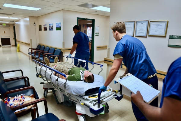 Emergency Department personnel at Naval Hospital Twentynine Palms conduct triage and initiate treatment on two role-playing Marines with simulated critical injuries during the Semper Durus 2025 regional training exercise, May 21. The casualties arrived via air medical evacuation following a notional explosion and friendly fire incident on Range 112, part of a mass casualty scenario coordinated with Marine Corps Air Ground Combat Center (MCAGCC) and other base tenants. After being transferred from the helipad by a corpsman and duty driver, the simulated patients were brought through the ambulance entrance, where medical teams activated the hospital’s Mass Casualty Protocol. The exercise provided a realistic test of interagency coordination, emergency medical response, and the hospital’s capacity to manage high-pressure incidents in real time (U.S. Navy photo by Christopher C. Jones, NHTP/NMRTC Twentynine Palms public affairs officer).