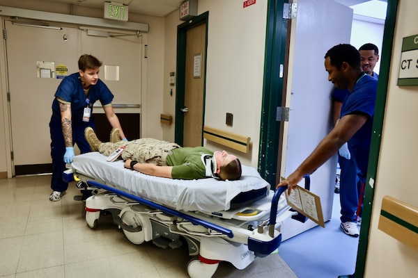 Emergency Department personnel at Naval Hospital Twentynine Palms conduct triage and initiate treatment on two role-playing Marines with simulated critical injuries during the Semper Durus 2025 regional training exercise, May 21. The casualties arrived via air medical evacuation following a notional explosion and friendly fire incident on Range 112, part of a mass casualty scenario coordinated with Marine Corps Air Ground Combat Center (MCAGCC) and other base tenants. After being transferred from the helipad by a corpsman and duty driver, the simulated patients were brought through the ambulance entrance, where medical teams activated the hospital’s Mass Casualty Protocol. The exercise provided a realistic test of interagency coordination, emergency medical response, and the hospital’s capacity to manage high-pressure incidents in real time (U.S. Navy photo by Christopher C. Jones, NHTP/NMRTC Twentynine Palms public affairs officer).