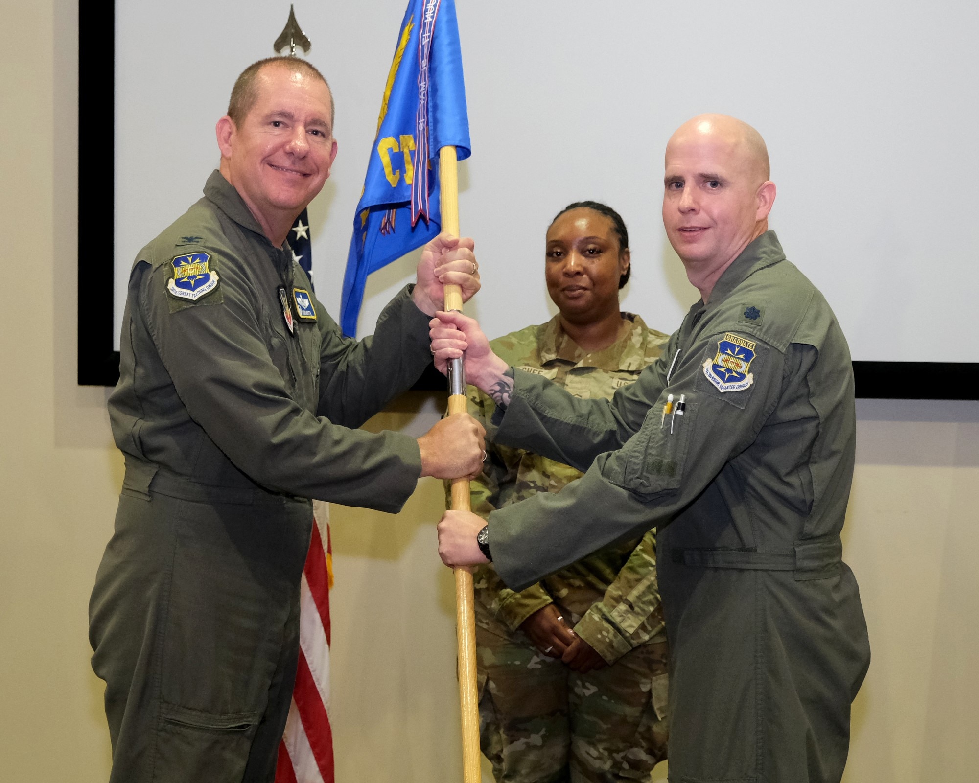 photo of three US Airmen standing on a stage, two Airmen are holding a unit flag