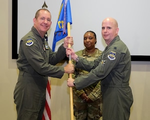 photo of three US Airmen standing on a stage, two Airmen are holding a unit flag