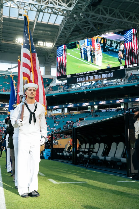 A U.S. Navy service member in the color guard stands at attention holding the American flag