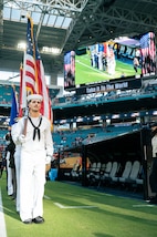 A U.S. Navy service member in the color guard stands at attention holding the American flag