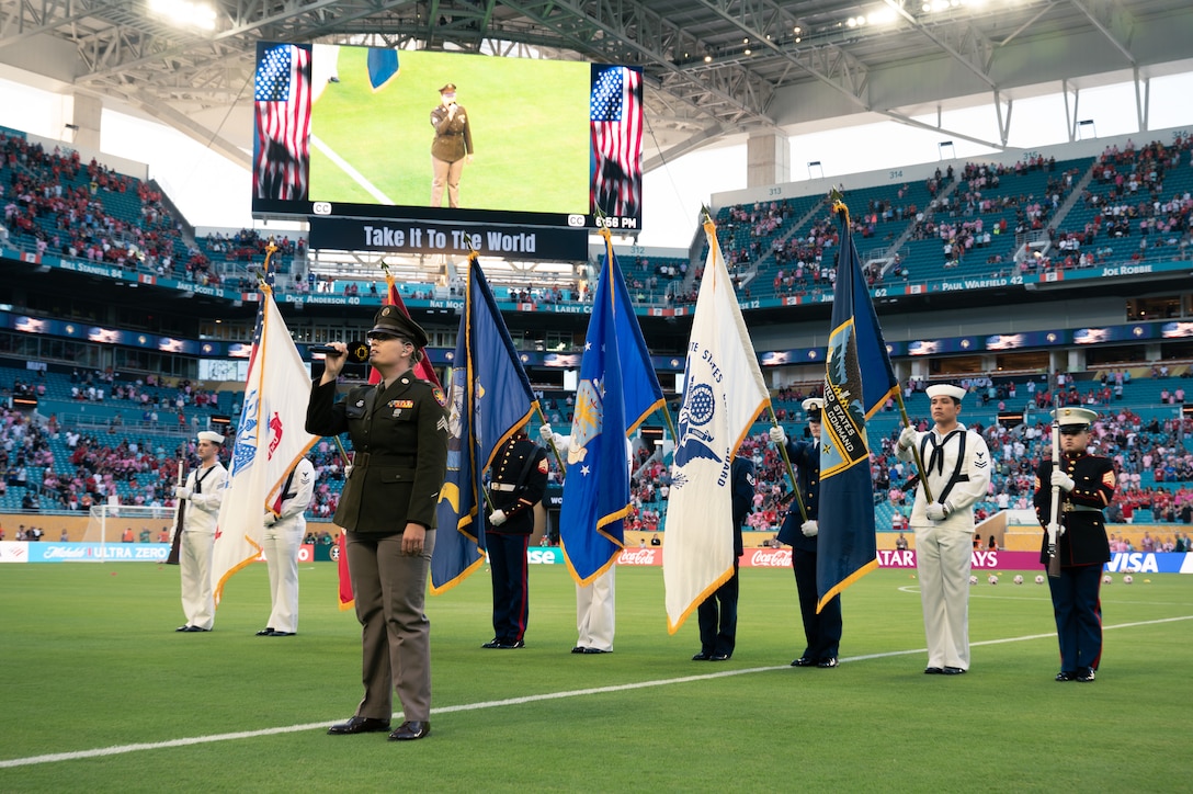 A U.S. Army service member sings the national anthem on the soccer field at Hard Rock Stadium while the color guard stands behind them