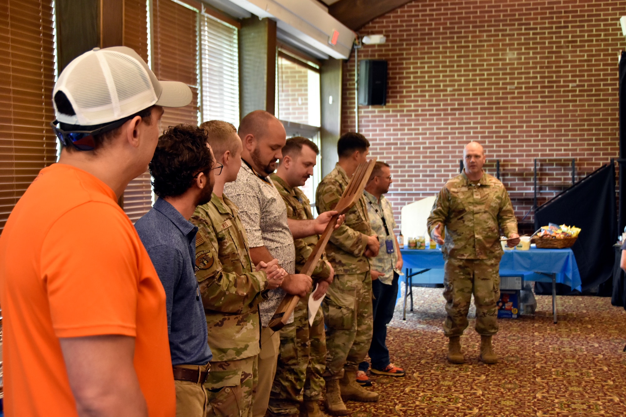 Col. Jason Vap, commander of the 804th Test Group, right, address 804th Test Group BBQ Cookoff contestants at the conclusion of the annual event, June 6, 2025, at the Arnold Lakeside Complex on Arnold Air Force Base, Tenn. During cookoff, several members of the 804th Test Group team vie for the coveted large wooden fork, the trophy given to the cookoff victor, by preparing barbecue which is not only shared with colleagues across the test group, but also judged by several others on the 804TG team. This year, Will Garner, test manager in the 804TG, pictured fourth from left, took home the top prize. (U.S. Air Force photo by Bradley Hicks)