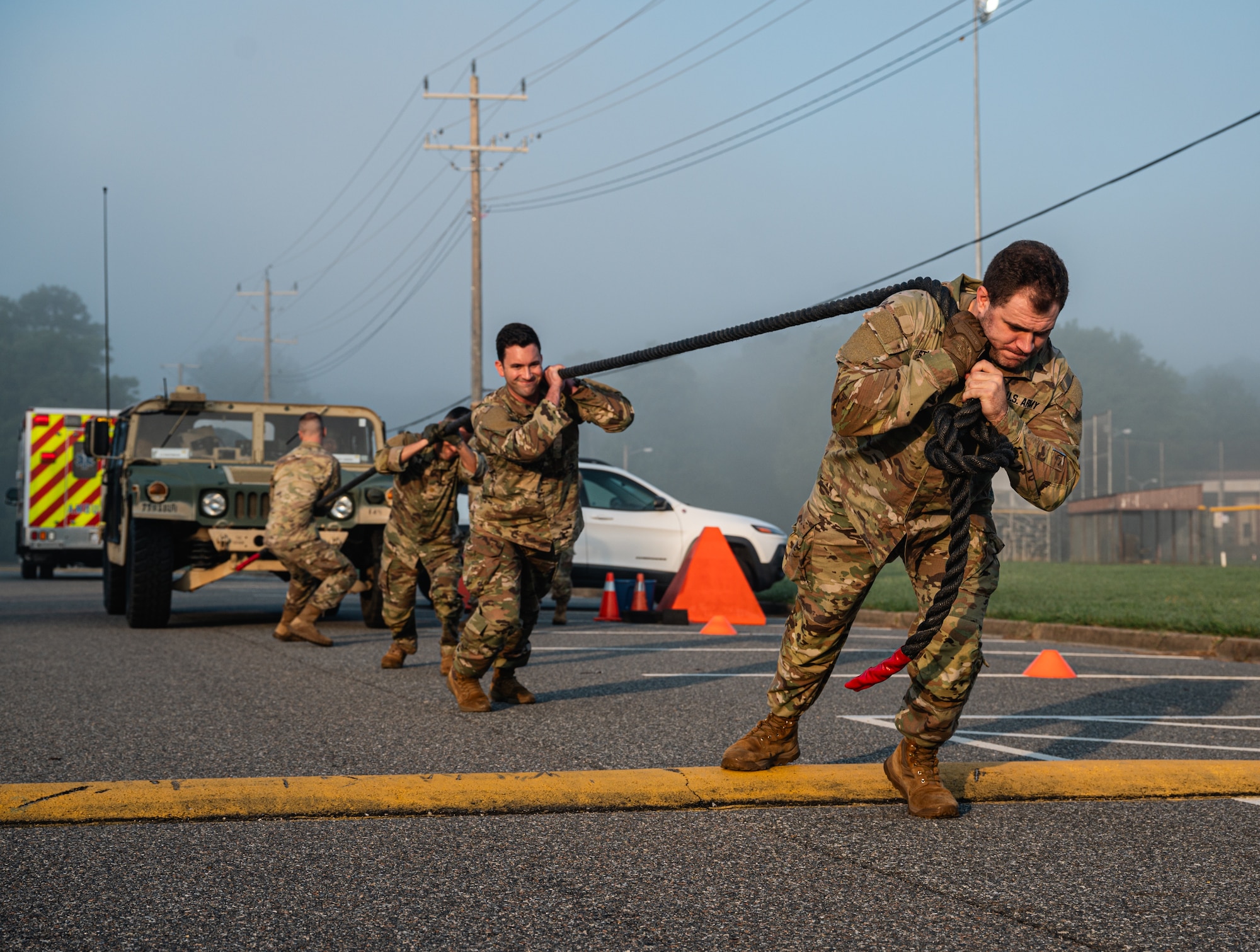 Four soldiers pull a humvee in uniform outside over a yellow speedbump