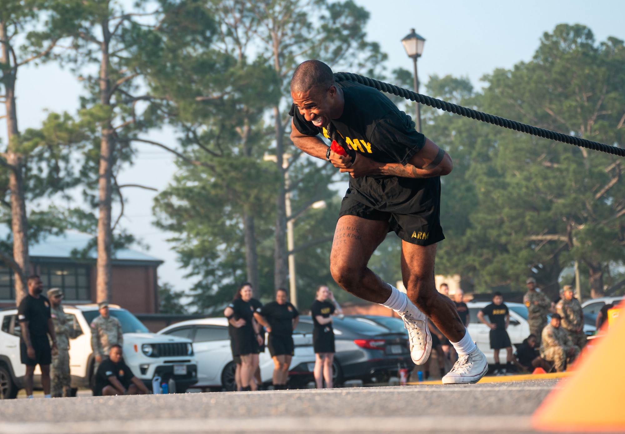 A soldier in a black pt uniform pulls a rope on pavement outside