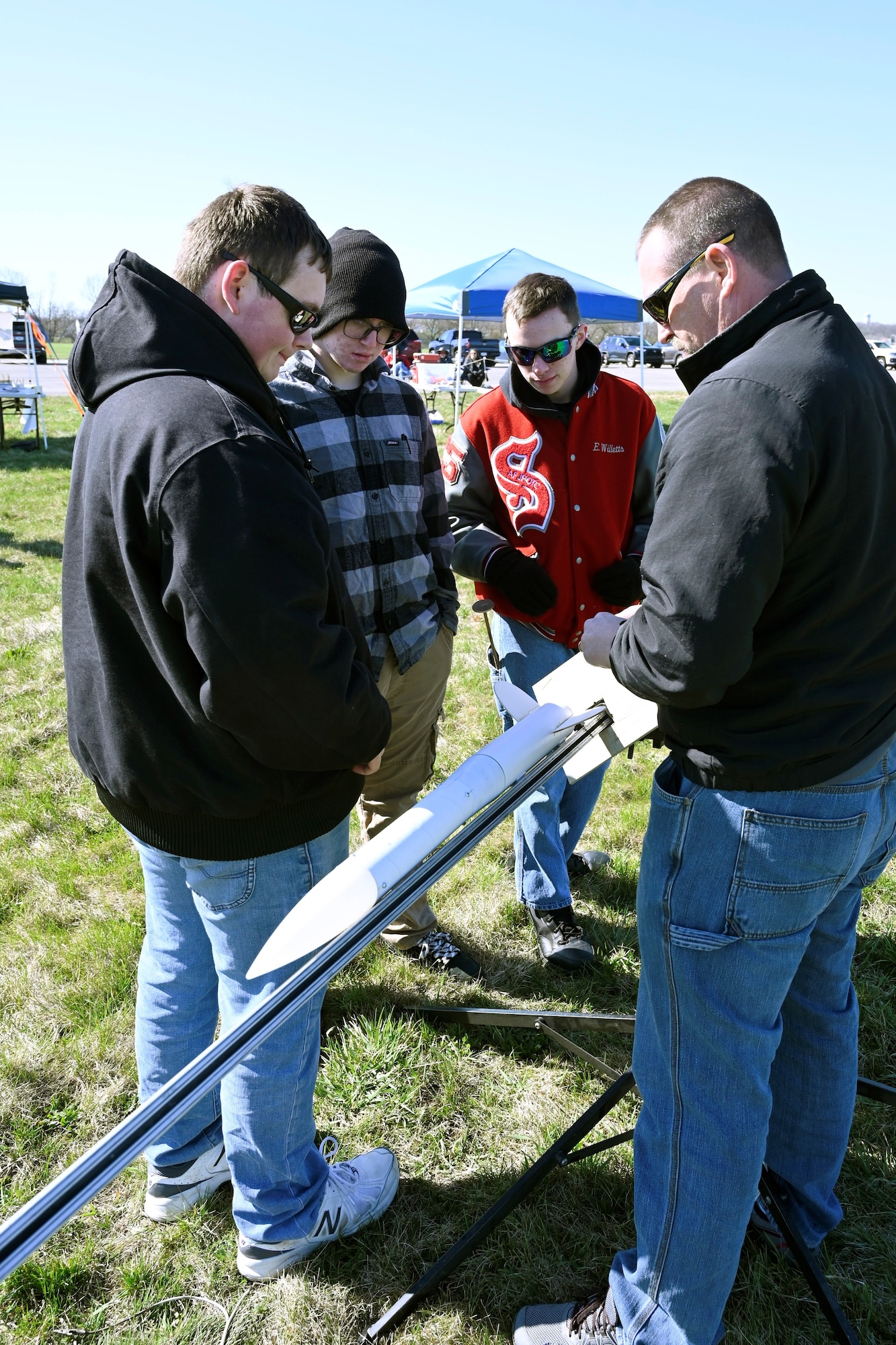 Three students standing with their instructor who is holding a 3- to 4-foot-long rocket in his hands.