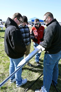 Three students standing with their instructor who is holding a 3- to 4-foot-long rocket in his hands.