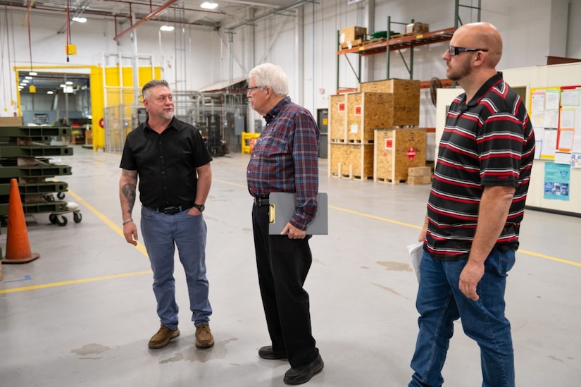 Three men stand in a large warehouse room.