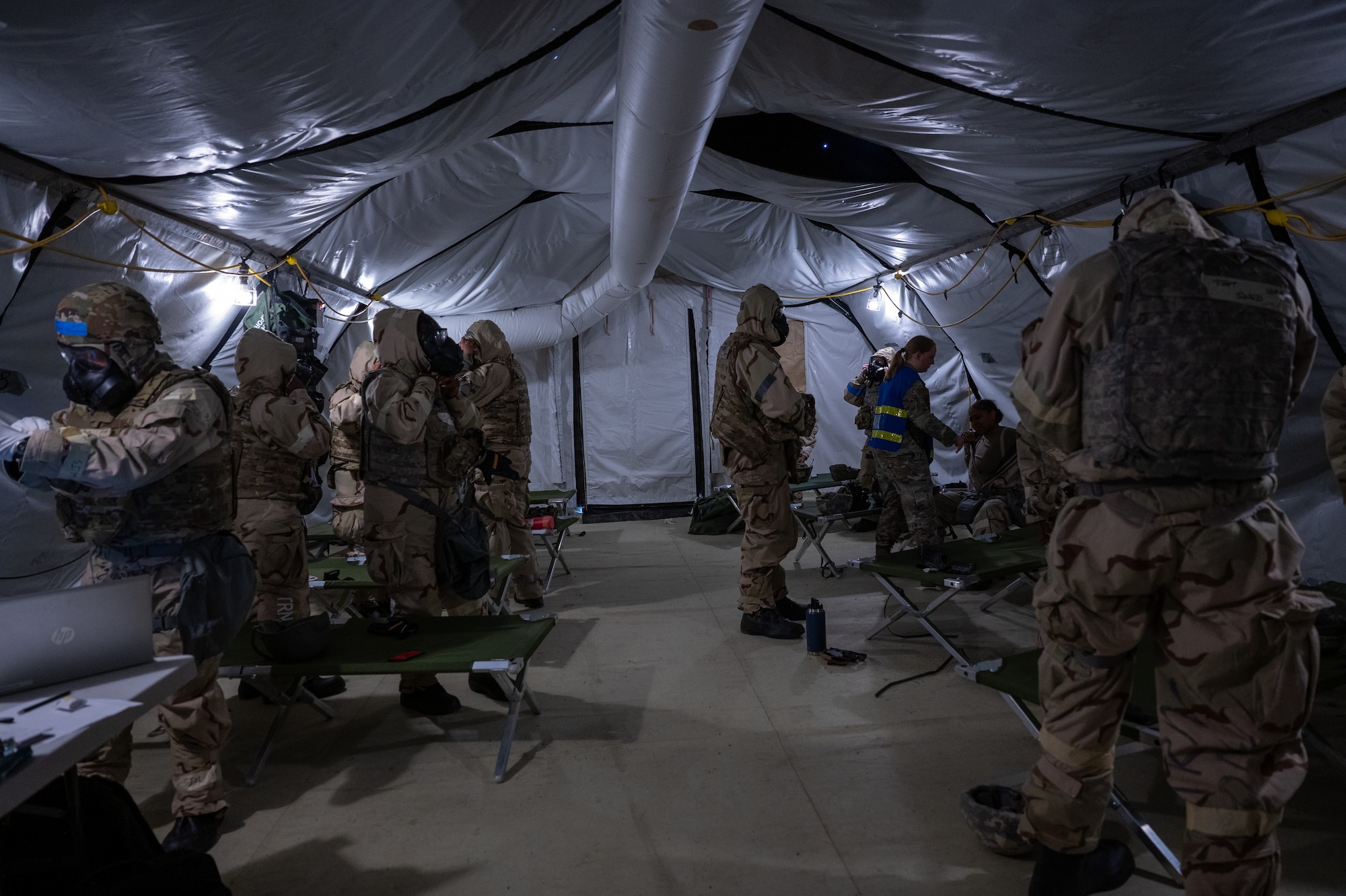 About a dozen Airmen are gearing up inside of a tent in MOPP 4.
