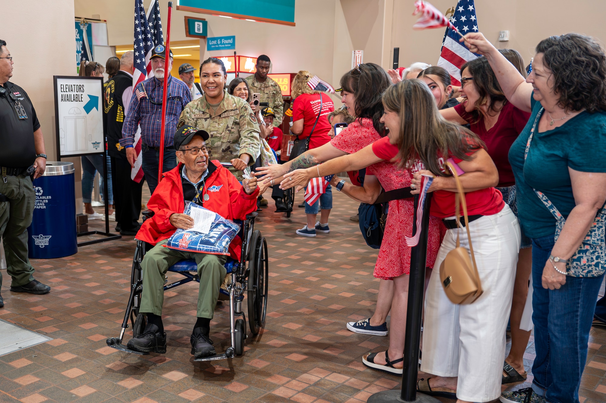A service member pushes a veteran in a wheelchair through a crowd