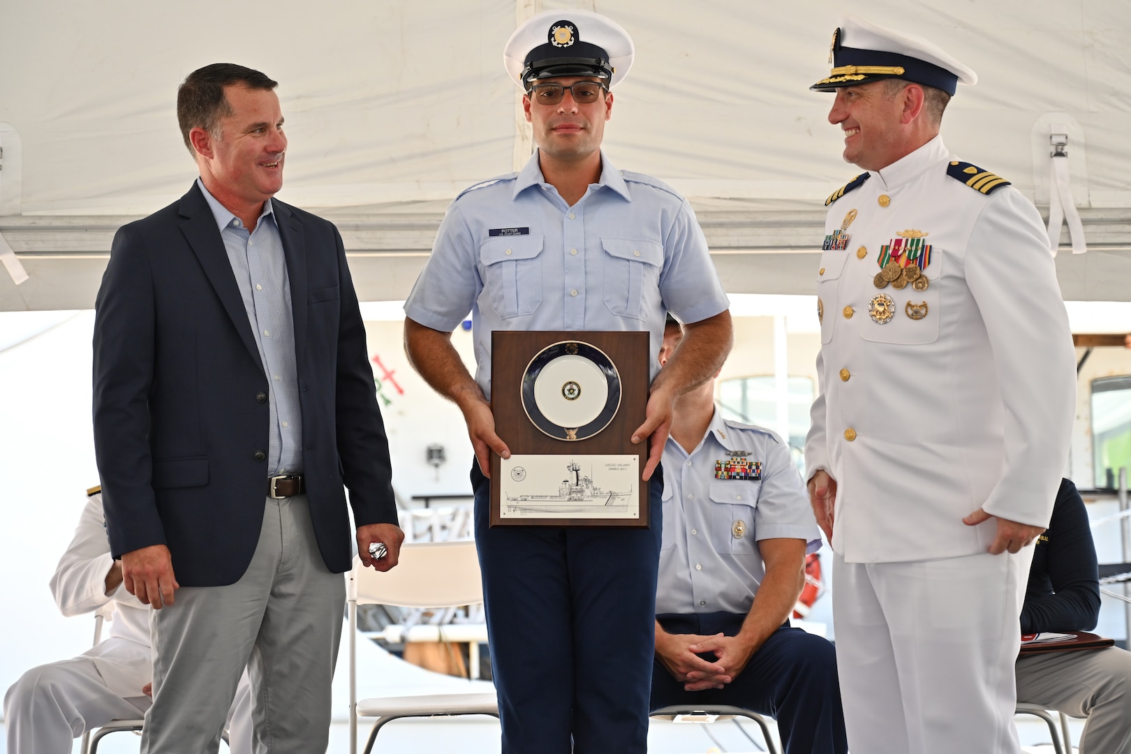 Cmdr. Matthew Press, commanding officer of Coast Guard Cutter Valiant (WMEC 621), and Seaman Grant Potter, a Valiant crew member, present retired Capt. Timothy Cronin, Valiant commanding officer, 2016-2018, a plaque during the cutter's heritage recognition ceremony in Jacksonville, Florida, June 17, 2024. The cutter was honored after more than 57 years of service in front of Coast Guard and cutter leadership, the assembled crew and former crew members, family and friends. (U.S. Coast Guard photo by Petty Officer 2nd Class Brandon Hillard)