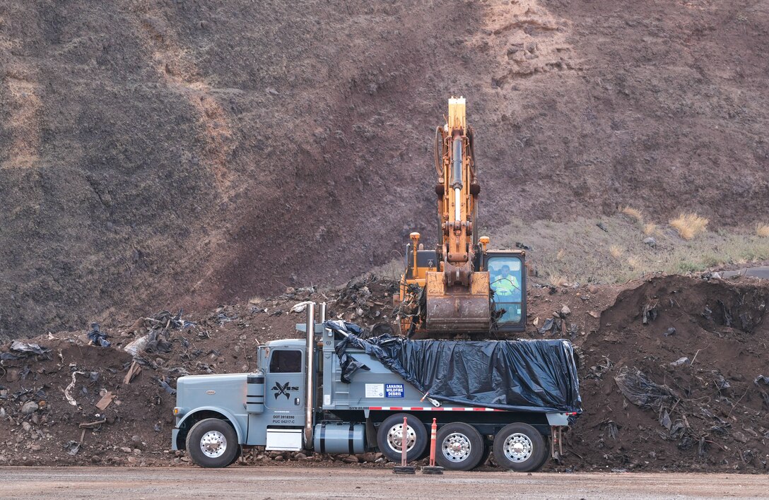 An excavator loads Lahaina wildfire debris into a dump truck at the Olowalu Temporary Debris Storage site before it is transported to the Permanent Disposal Site adjacent to the Central Maui Landfill in Puʻunēnē June 16, 2025. A total of approximately 400,000 tons of debris will be moved to the permanent site over five months. (Photo Courtesy of Nicole Timon-Shipman, Federal Emergency Management Agency Public Affairs).