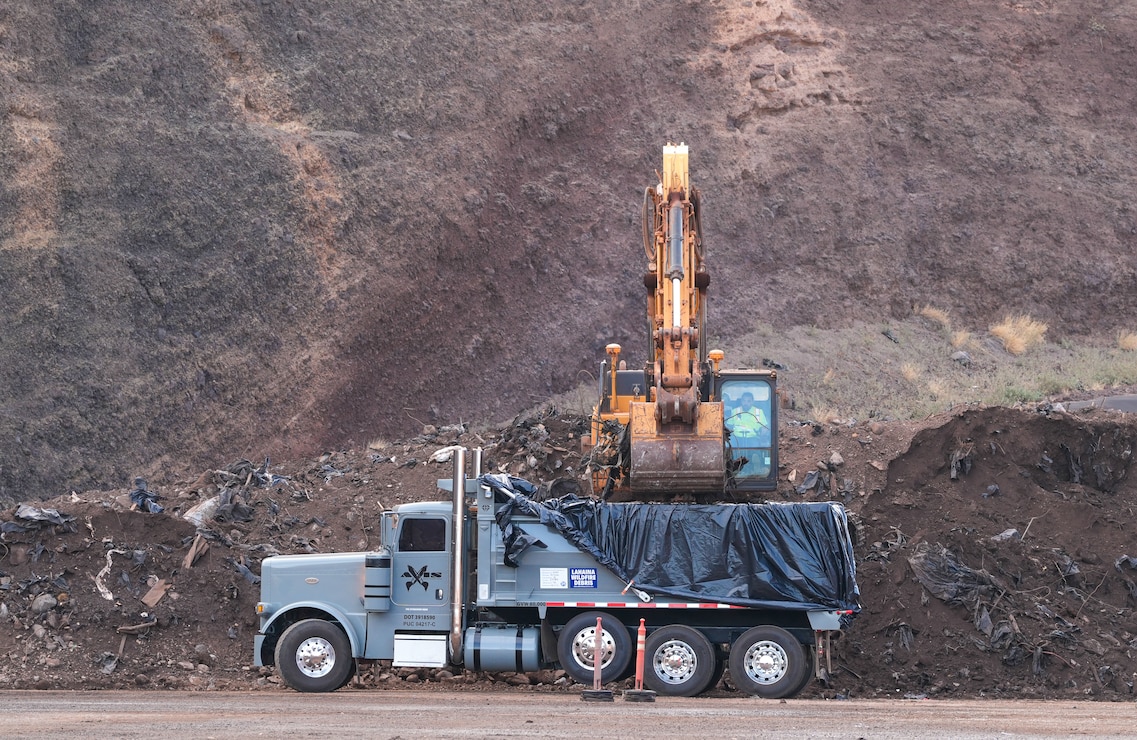 An excavator loads Lahaina wildfire debris into a dump truck at the Olowalu Temporary Debris Storage site before it is transported to the Permanent Disposal Site adjacent to the Central Maui Landfill in Puʻunēnē June 16, 2025. A total of approximately 400,000 tons of debris will be moved to the permanent site over five months. (Photo Courtesy of Nicole Timon-Shipman, Federal Emergency Management Agency Public Affairs).