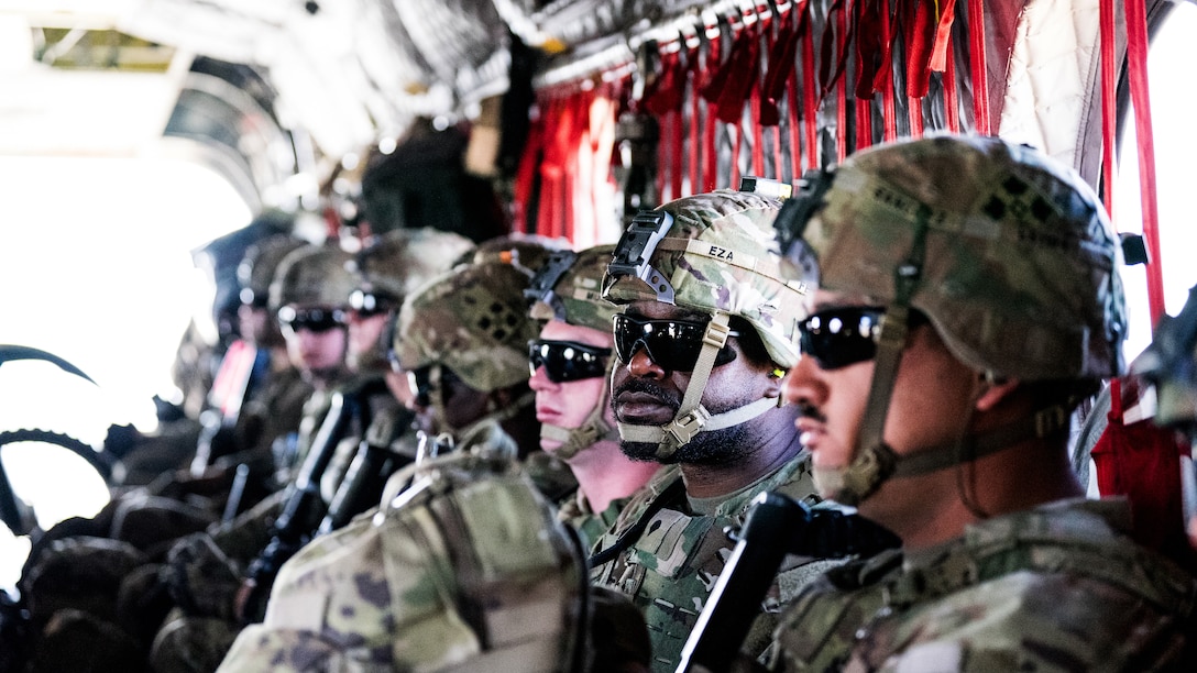 Soldiers and Border Patrol agents are seen sitting in an aircraft with sunlight at the rear.