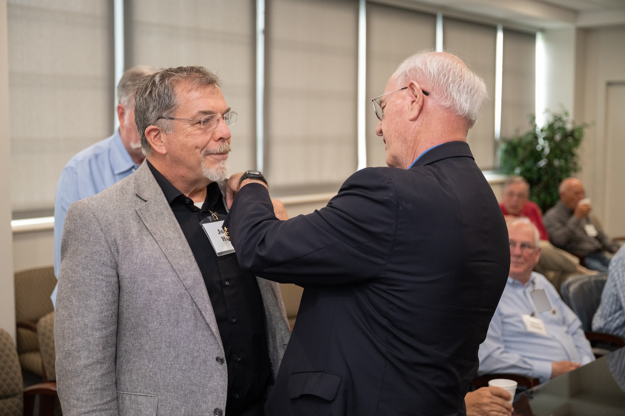 Newly selected Arnold Engineering Development Complex Fellow John Hopf, left, receives his AEDC Fellows lapel pin from Maj. Gen. (Ret.) Mike Wiedemer with the Arnold Community Council during AEDC Fellows Day June 17, 2025, at Arnold Air Force Base, Tenn. AEDC is headquartered at Arnold AFB. Hopf was one of the three AEDC retirees selected by the ACC for induction into the Fellows program this year. The AEDC Fellows program recognizes AEDC personnel who have made substantial and exceptionally distinguished contributions to the nation’s aerospace ground testing capability. Newly selected AEDC Fellows are traditionally honored annually on or around June 25 to coincide with the birthday of Gen. Henry “Hap” Arnold and anniversary of the June 1951 dedication of AEDC in Gen. Arnold’s honor. (U.S. Air Force photo by Keith Thornburgh) (This image was altered by obscuring badges for security purposes)