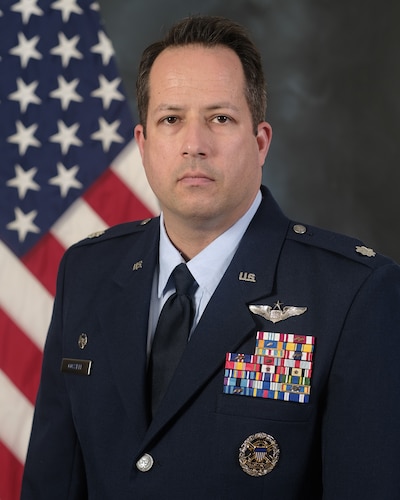 photo of uniformed US Airman standing in front of a US Flag.