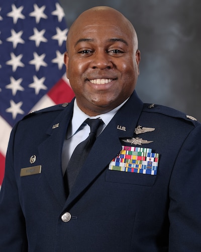 photo of uniformed US Airman standing in front of a US Flag.