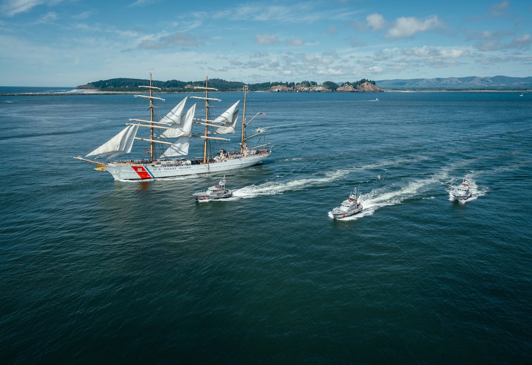 A ship sails left next to three boats under a partly sunny sky.
