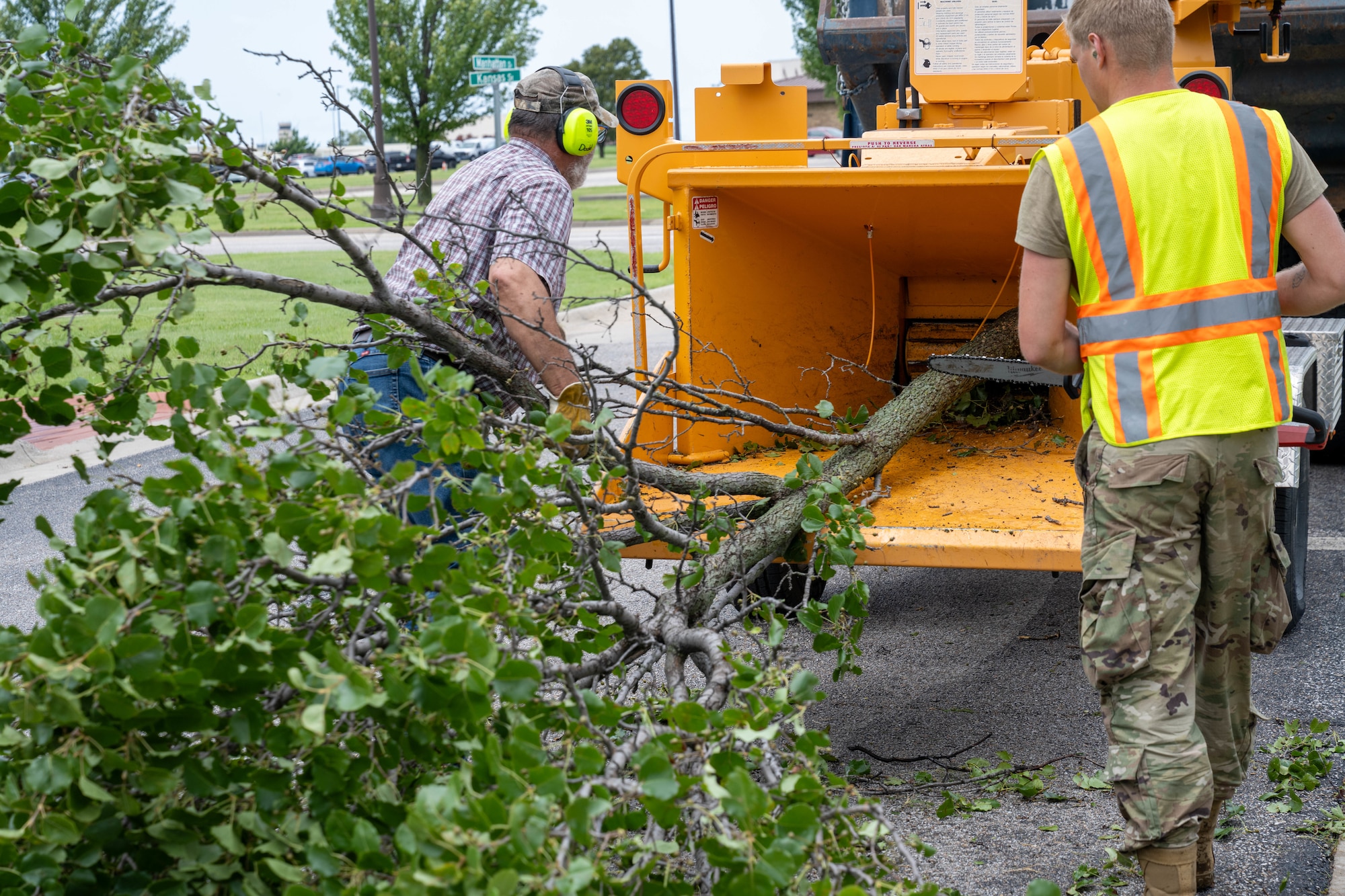 Two Team McConnell members feed a branch into a woodchipper