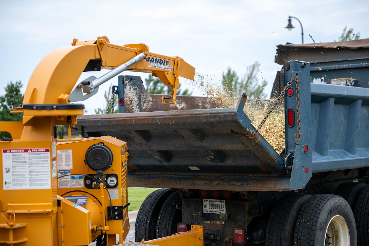 A woodchipper empties into the back of a truck
