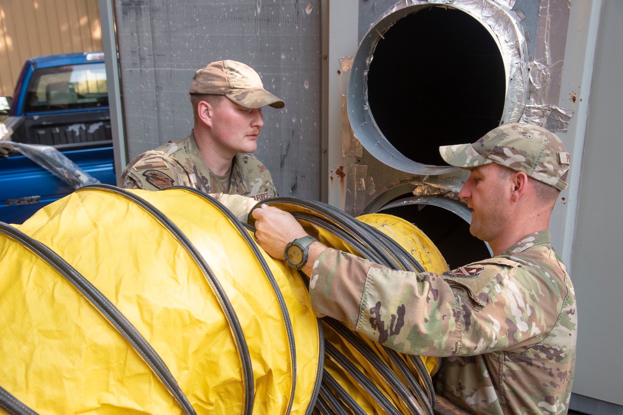 U.S. Air Force Staff Sgt. Jacob V. Myers and Tech Sgt. Daniel R. Plefka, 316th Civil Engineer Squadron heating, ventilation and air conditioning shop, connect ducting to a mobile HVAC unit outside the Tactical Fitness Center at Joint Base Andrews, Md., June 11, 2025. Members of the 316th CES set up power and HVAC units for U.S. Army Soldiers staging at the fitness center for the Army’s 250th Birthday Festival and Parade in Washington, D.C.