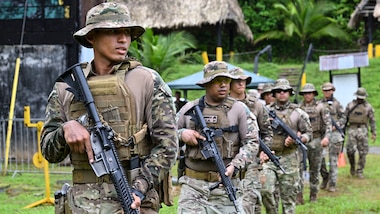 Panamanian service members and U.S. Marines walk in a single filed line carrying guns