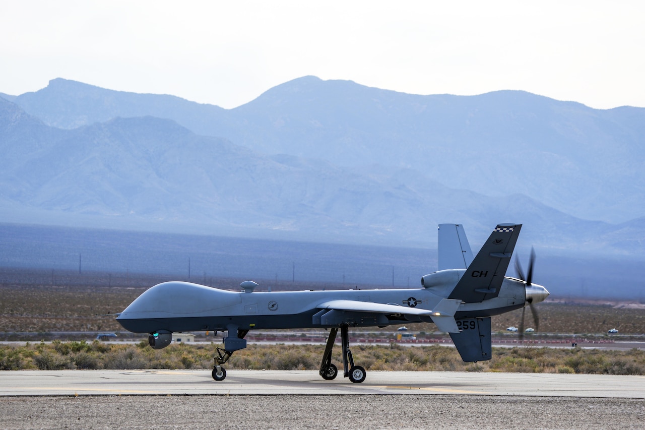 An aircraft moves along paved ground. Mountains are in the background.
